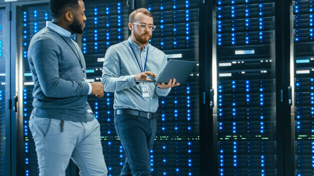 IT Technician with a Laptop Computer and Black Male Engineer Colleague are Talking in Data Center